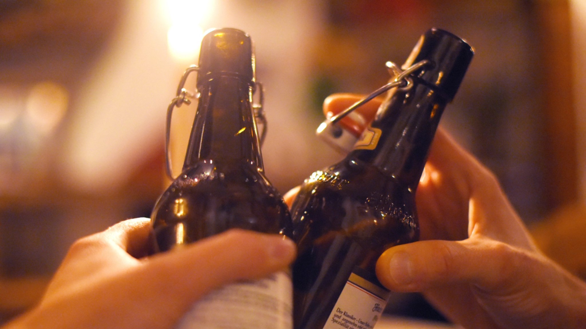 Zwei Menschen stoßen mit Bierflaschen an (Symbolbild).