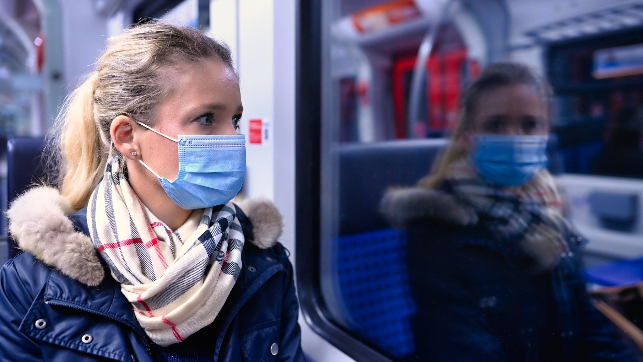 Frau sitzt in der S-Bahn und sieht nachdenklich nach draußen, sie spiegelt sich im Fenster.