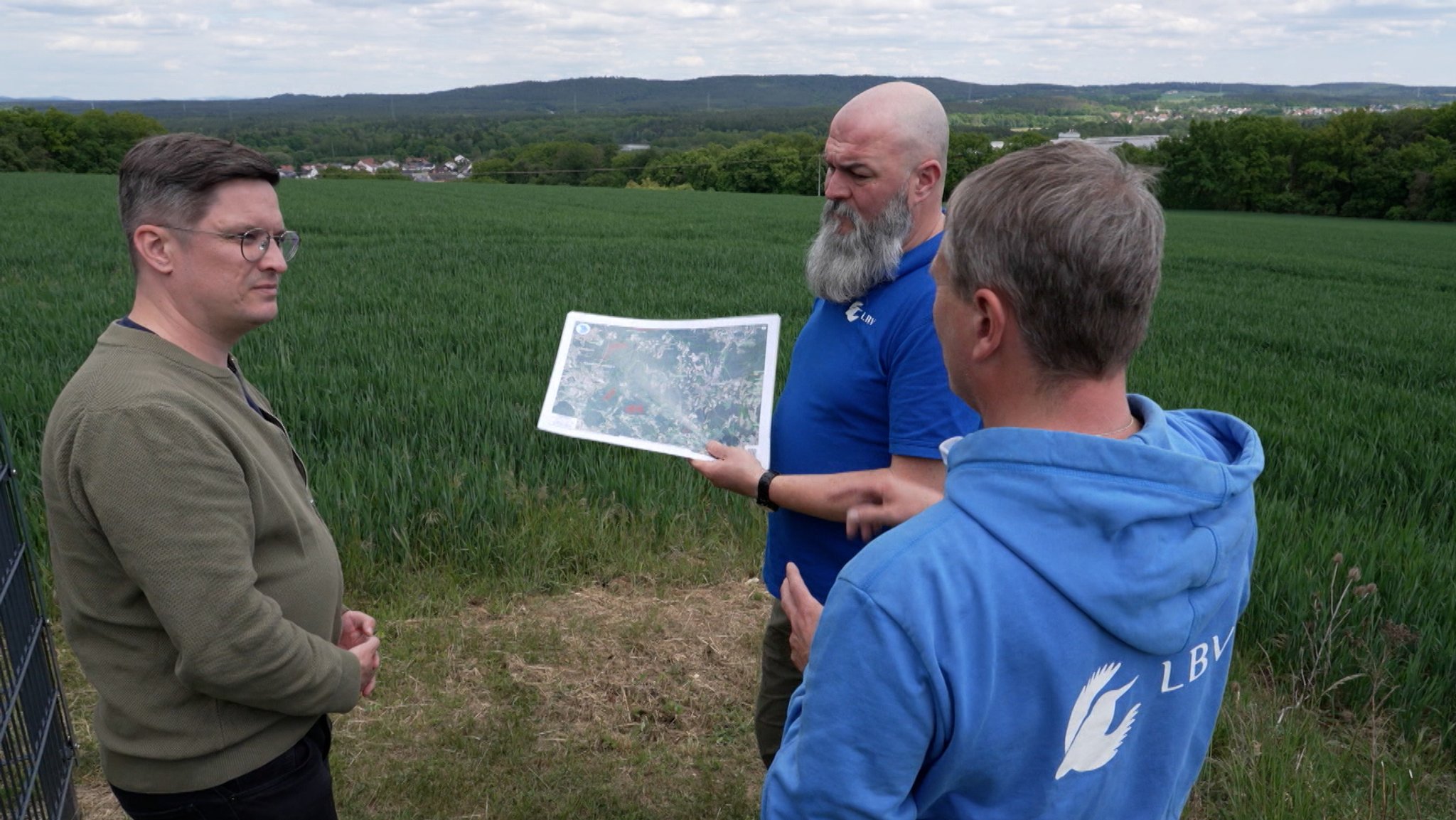 Auf dem Bild ist eine Gruppe von drei Männern zu sehen, die im Kreis steht und miteinander diskutiert. | Bild: Bayerischer Rundfunk 2026 Auf dem Bild ist eine Gruppe von drei Männern zu sehen, die im Kreis steht und miteinander diskutiert.