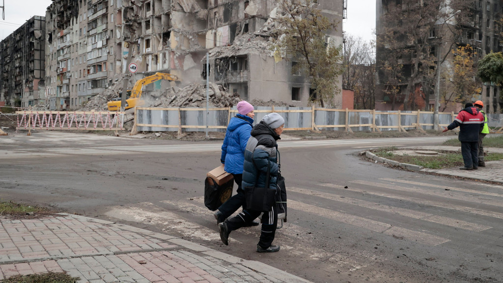 Mariupol: Menschen gehen mit Taschen an Gebäuden vorbei, die durch Kämpfe beschädigt wurden. 