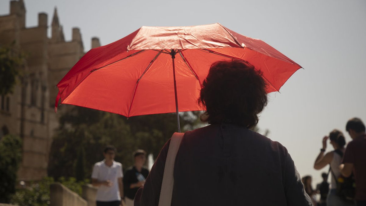 19.07.2023, Spanien, Palma: Eine Frau mit einem Regenschirm geht an der Kathedrale vorbei. Foto: Clara Margais/dpa +++ dpa-Bildfunk +++