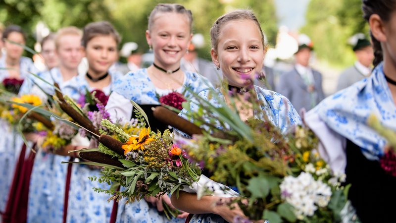 In Tracht gekleidete Mädchen mit Kräuterbuschen nehmen am Trachtenfestzug durch den Ort Kochel am See zu Maria Himmelfahrt 2019 teil.