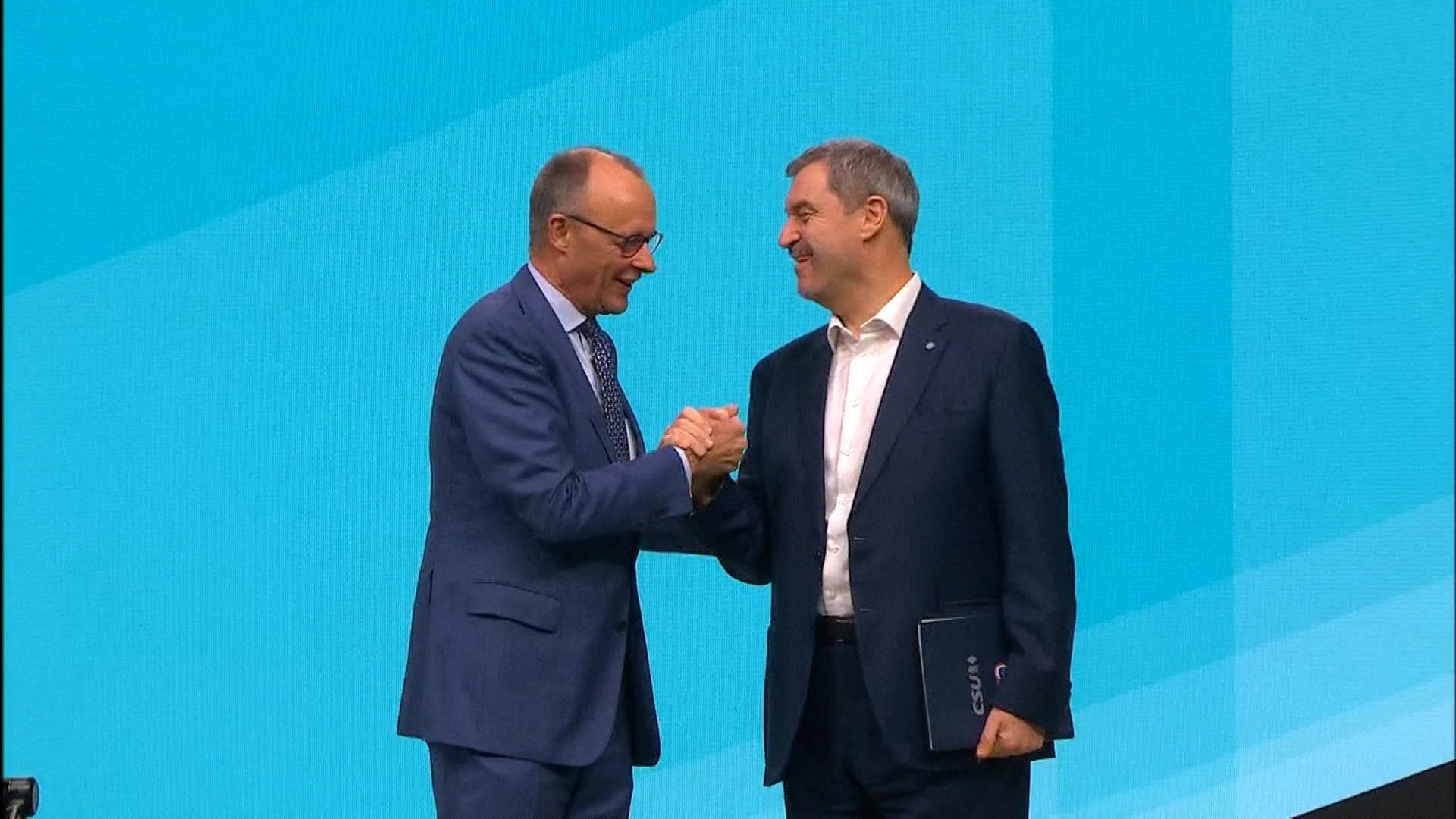 Friedrich Merz und Markus Söder geben sich auf der Bühne die Hand