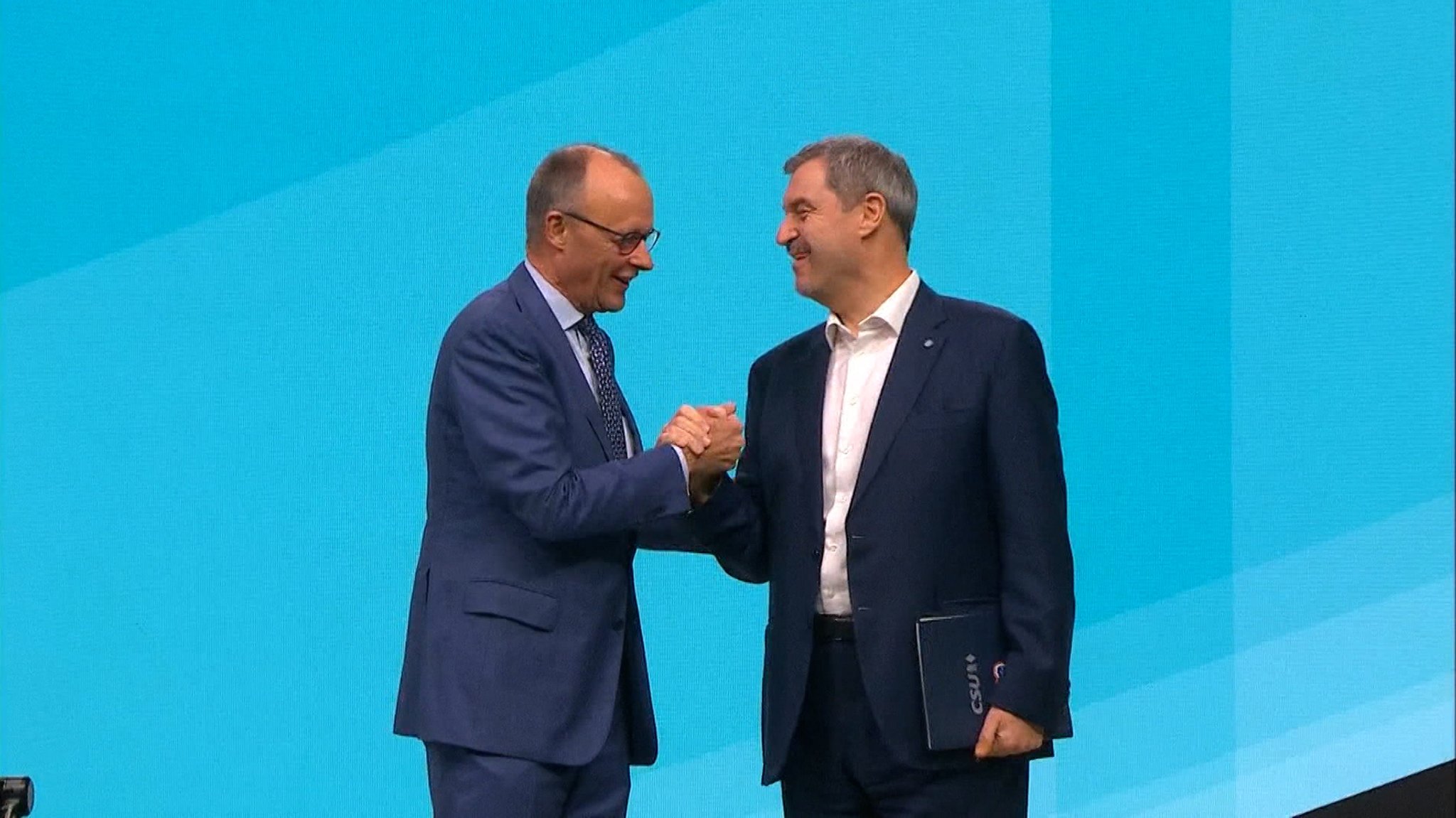 Friedrich Merz und Markus Söder geben sich auf der Bühne die Hand