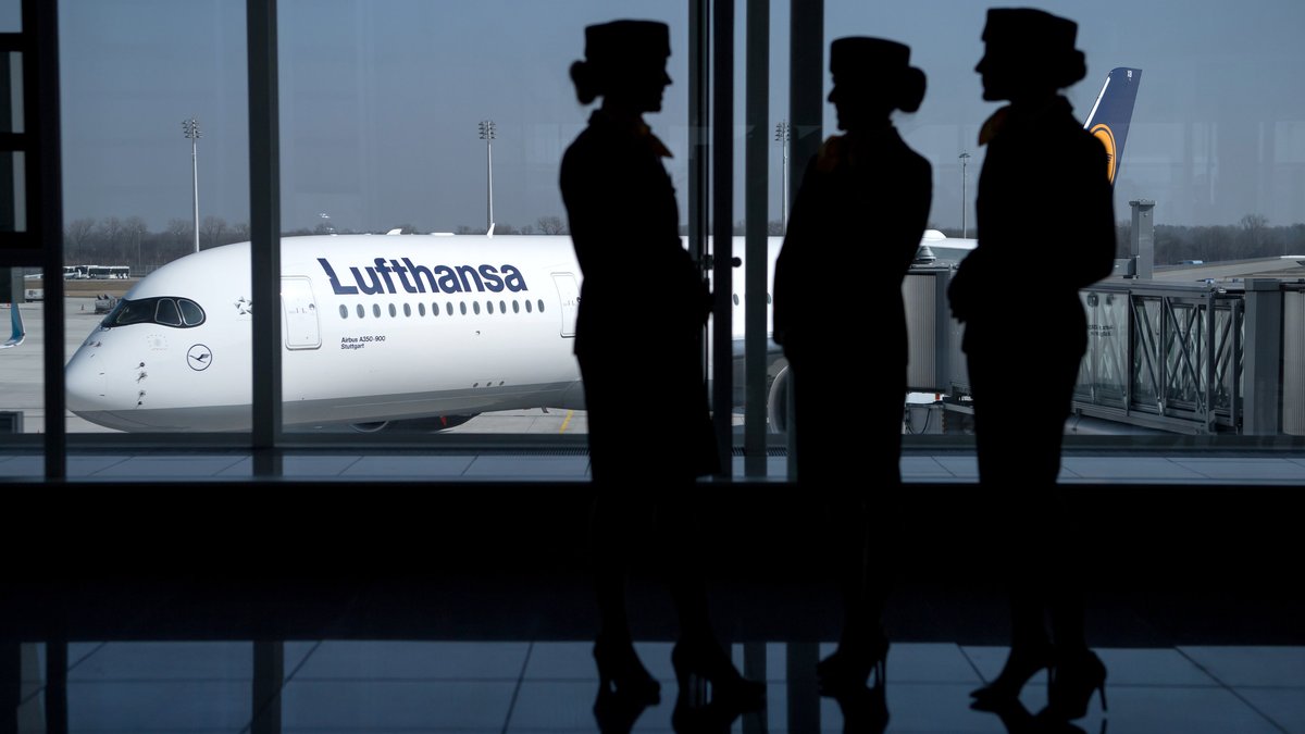 Flugbegleiterinnen der Deutschen Lufthansa AG stehen am Flughafen in München, im HIntergrund ein Lufthansa-Flugzeug