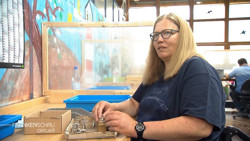 Eine Frau steckt in einer Werkstatt für Menschen mit Behinderung Metallteile zusammen.