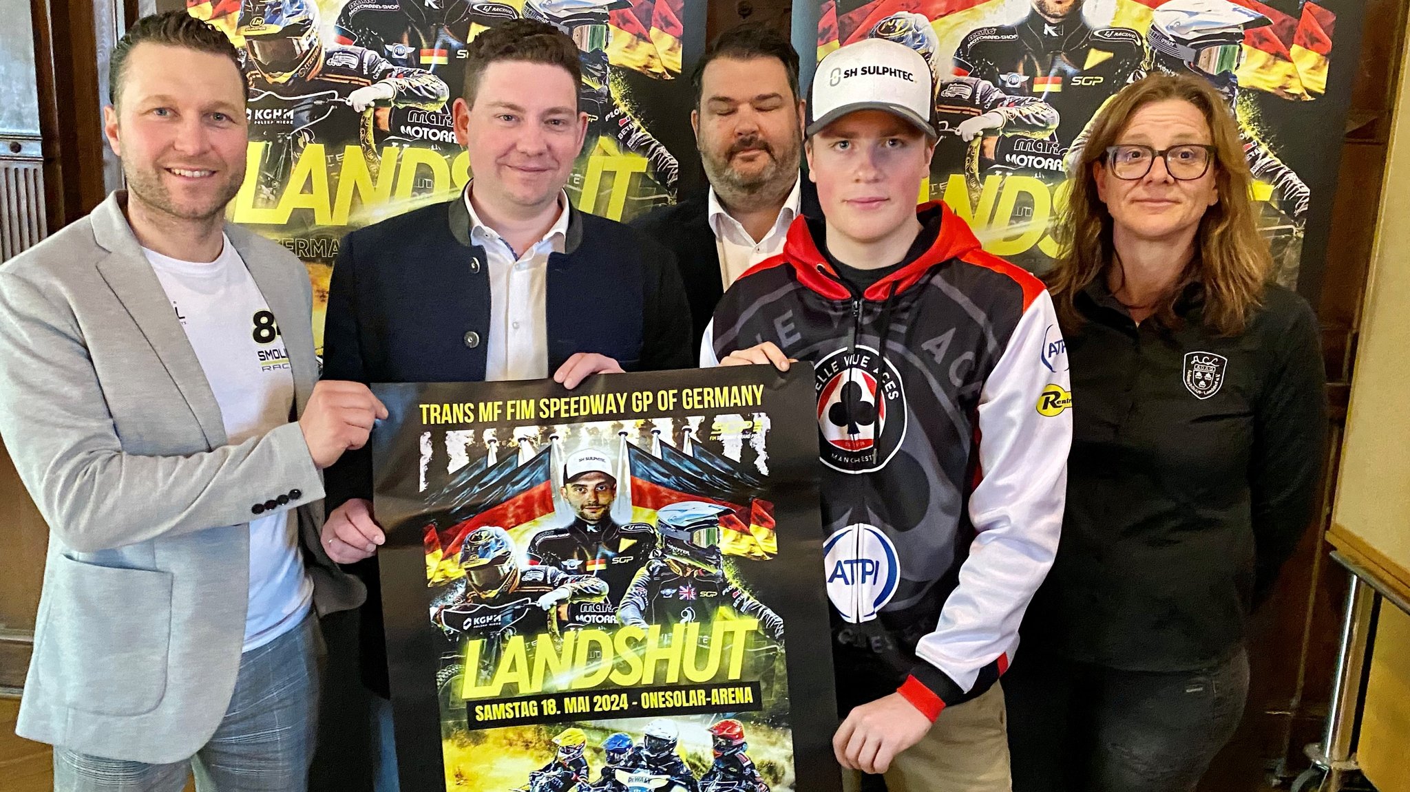 Teilnehmer und Veranstalter des Speedway-Grand Prix halten ein Plakat hoch. 