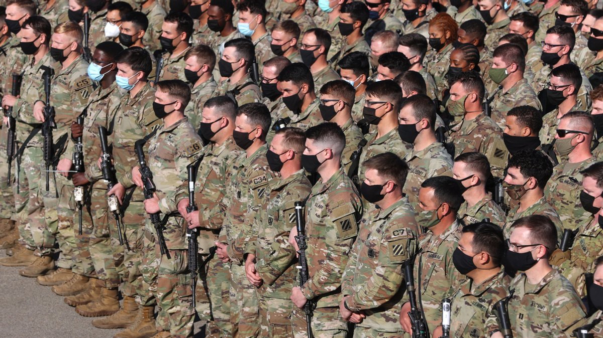 Soldaten der US-Armee in Tarnanzügen, mit Gewehren und Mundschutz in Reih und Glied.