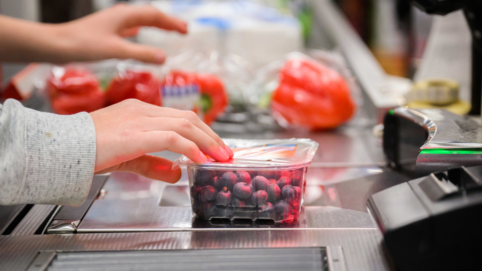 Eine Kassiererin scannt Heidelbeeren an der Kasse eines Supermarktes.