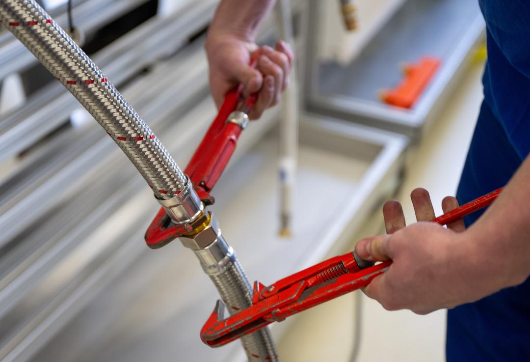 Symbolbild: Ein Handwerker verbindet zwei Schläuche mit Zangen.