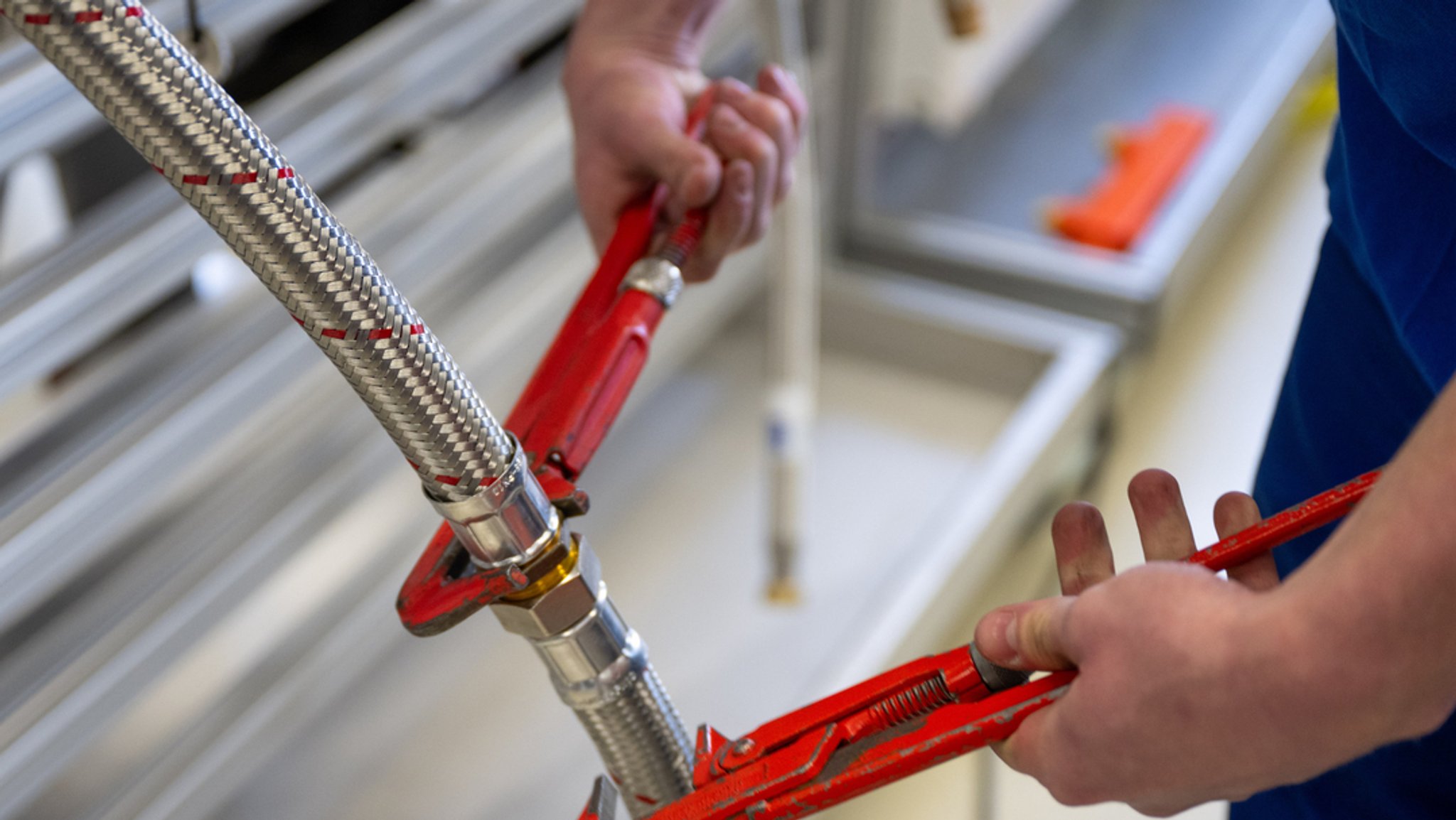 Symbolbild: Ein Handwerker verbindet zwei Schläuche mit Zangen.