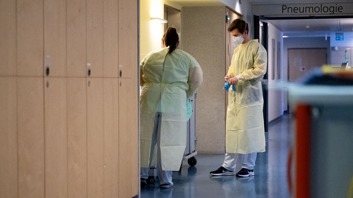 Eine Krankenpflegerin und ein Oberarzt ziehen vor einem Patientenzimmer einer Covid-19-Station in einem Krankenhaus Schutzkleidung an. 