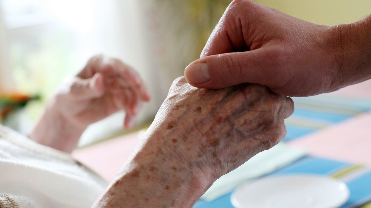 Ein Pfleger hält in einem Pflegeheim die Hand einer Bewohnerin.