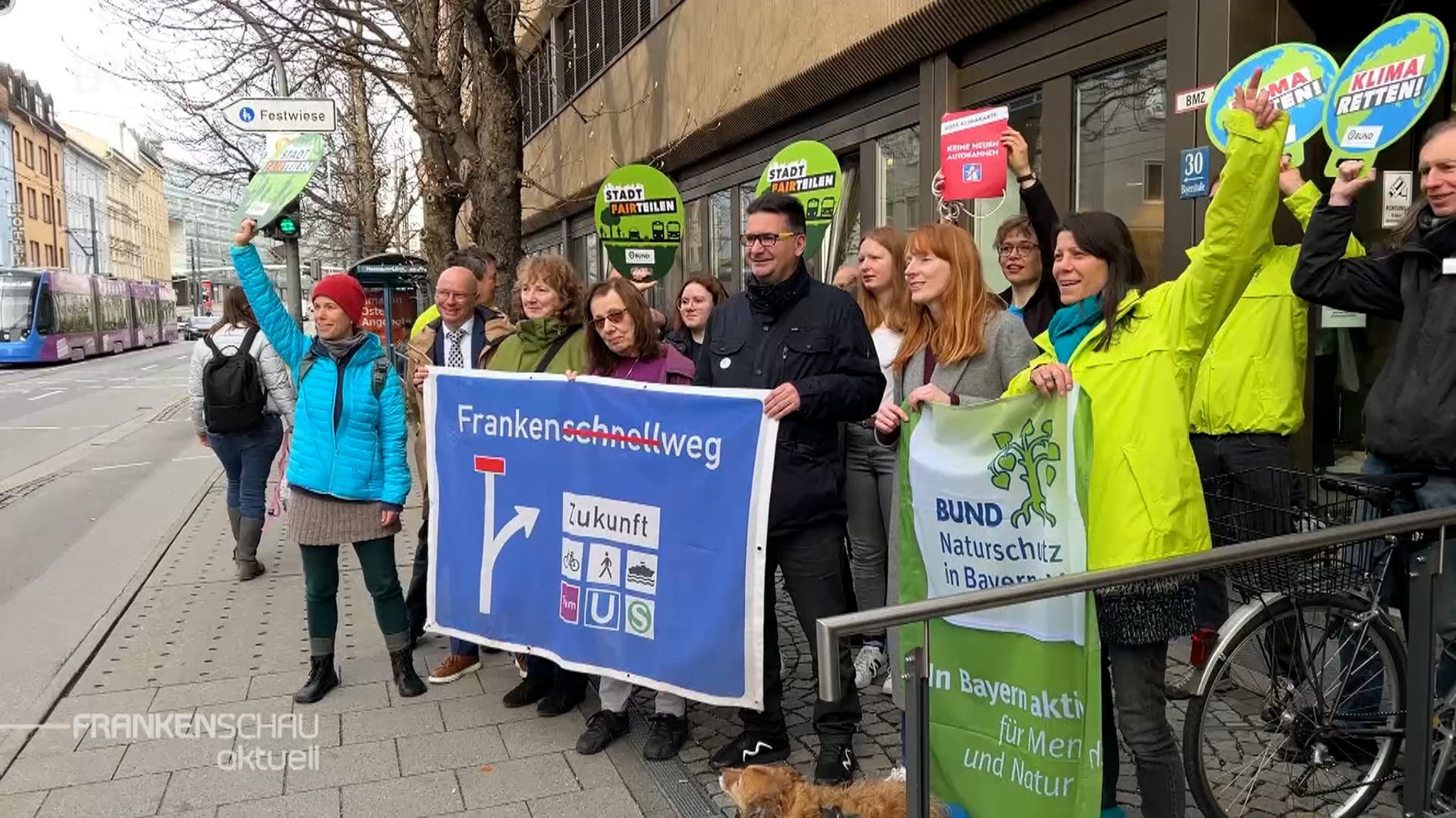 Demonstranten und Demonstrantinnen mit Protestschildern am Straßenrand.