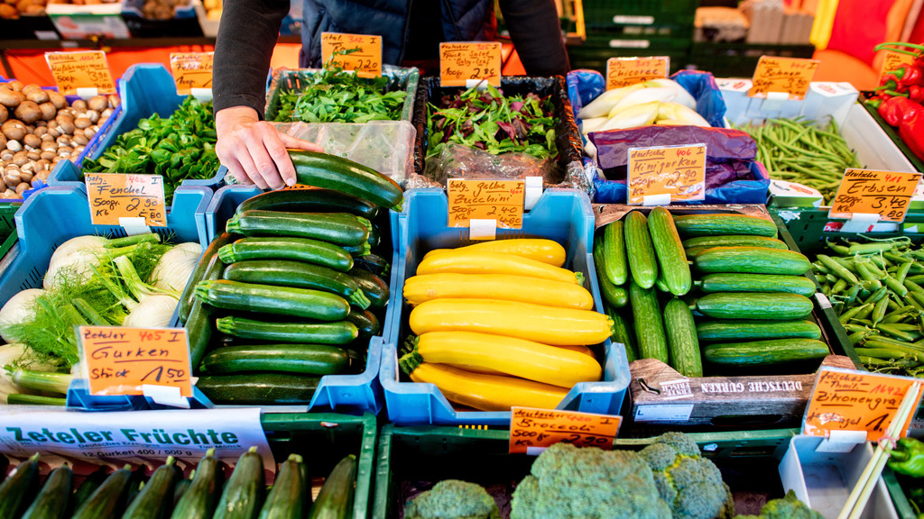 Ein Verkäufer greift an einem Obst- und Gemüsestand auf dem Wochenmarkt in eine Kiste mit Zucchini. Das Leben in Deutschland hat sich in den vergangenen Monaten spürbar verteuert. So hoch war die Inflationsrate seit Jahrzehnten nicht mehr.