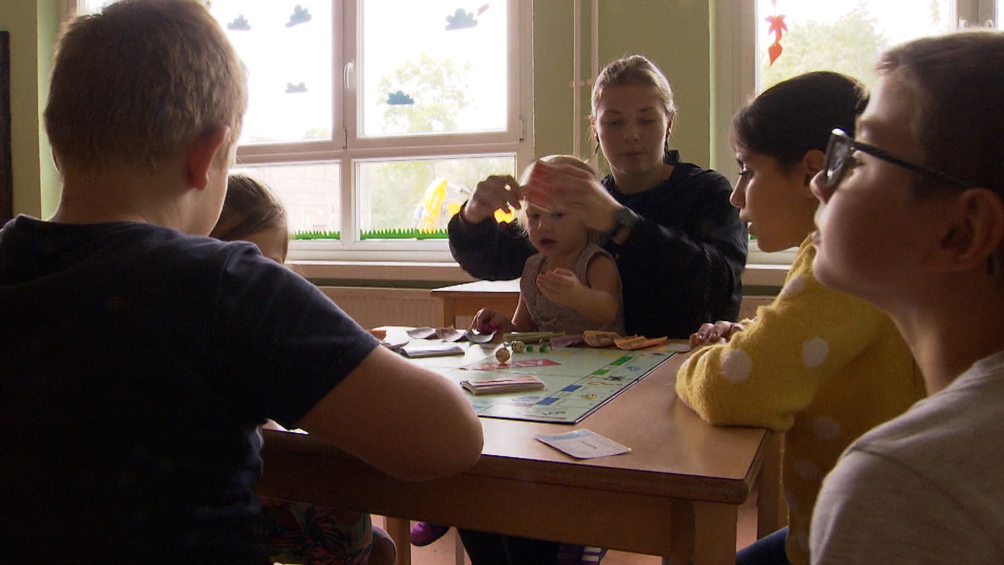 Kinder spielen Monopoly an einem Tisch.