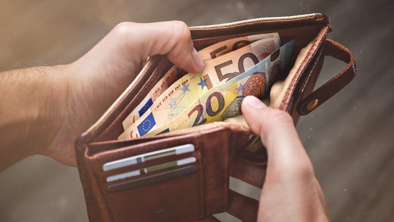 Ein Mann öffnet einen Geldbeutel. | Bild: stock.adobe.com/photoschmidt Ein Mann öffnet einen Geldbeutel.