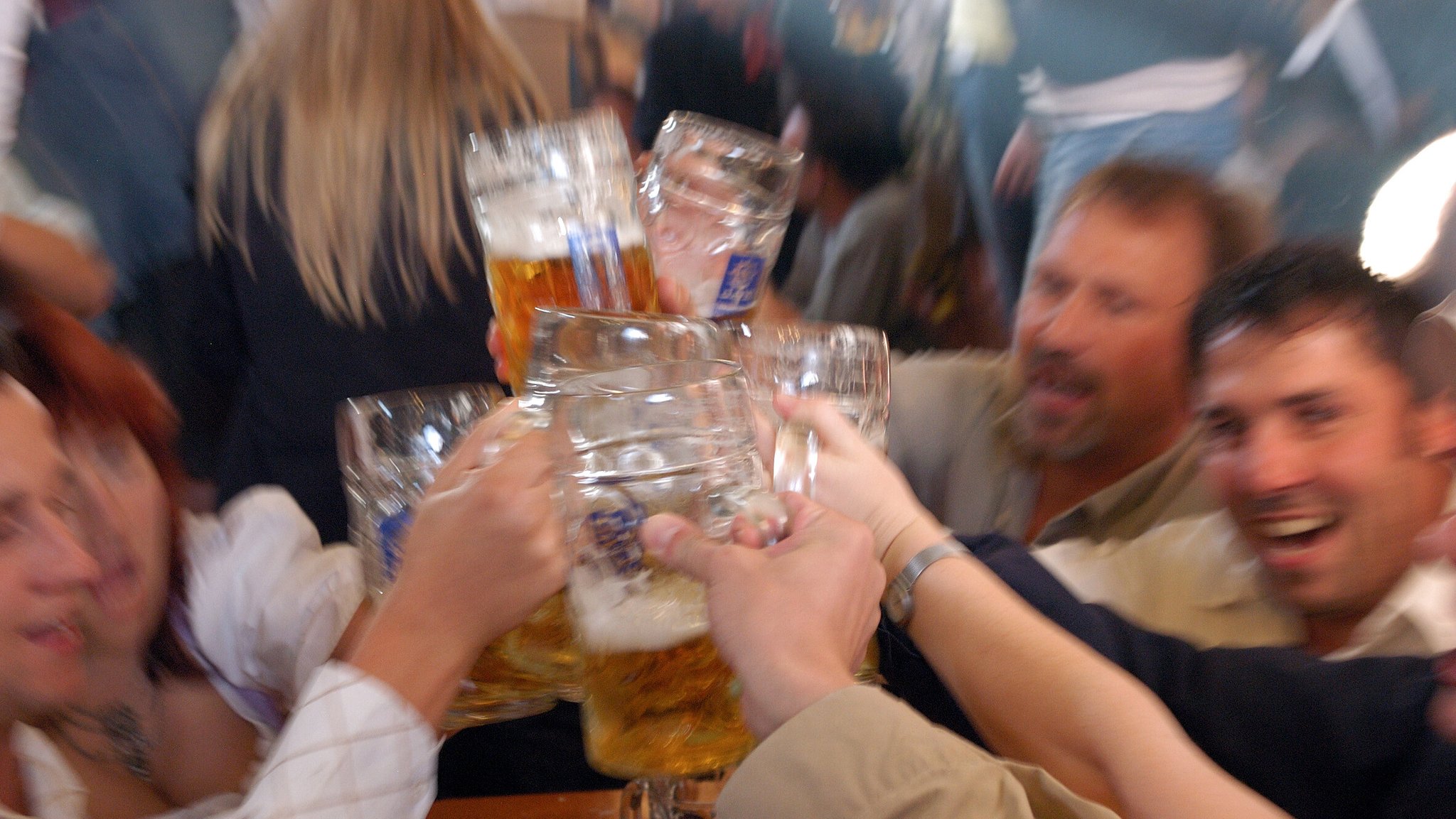 (Symbolbild) Feiernde Menschen prosten sich mit Bierkrügen zu. 