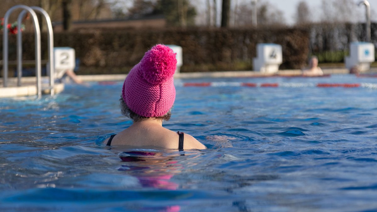 Eine Frau mit Pudelmütze schwimmt im Schwimmbad.
