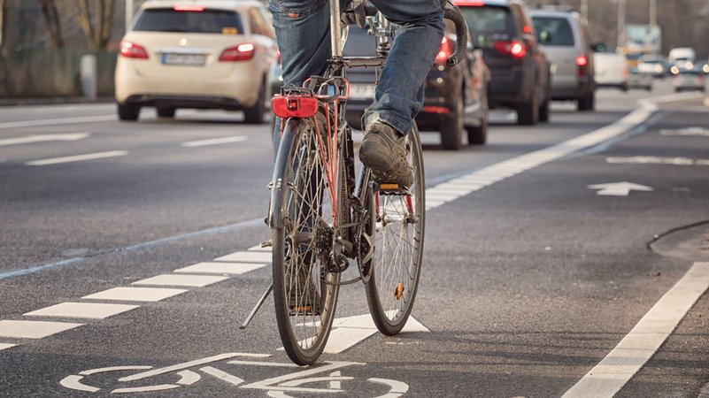 Ein Fahrradfahrer fährt im Straßenverkehr auf einer Fahrradspur neben Autos