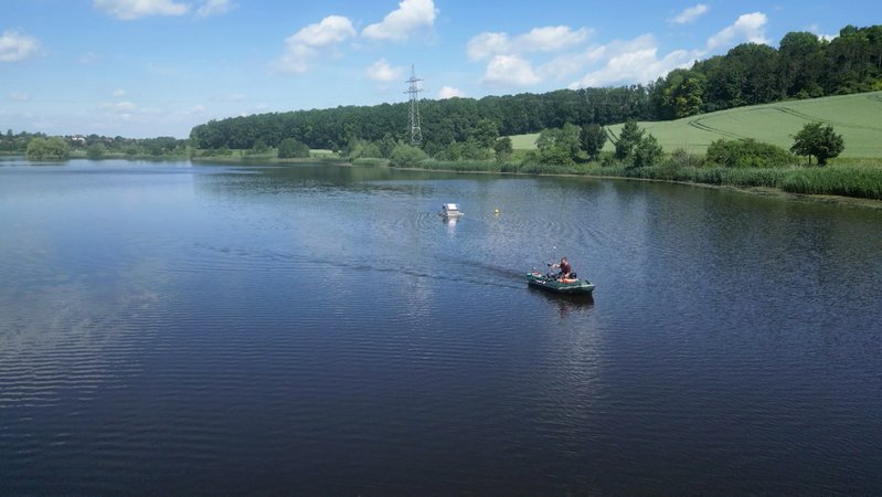 Auf einem großen See, an dessen Ufer grüne Bäume und Felder zu sehen sind, ist ein Boot unterwegs. | Bild: BR Auf einem großen See, an dessen Ufer grüne Bäume und Felder zu sehen sind, ist ein Boot unterwegs.