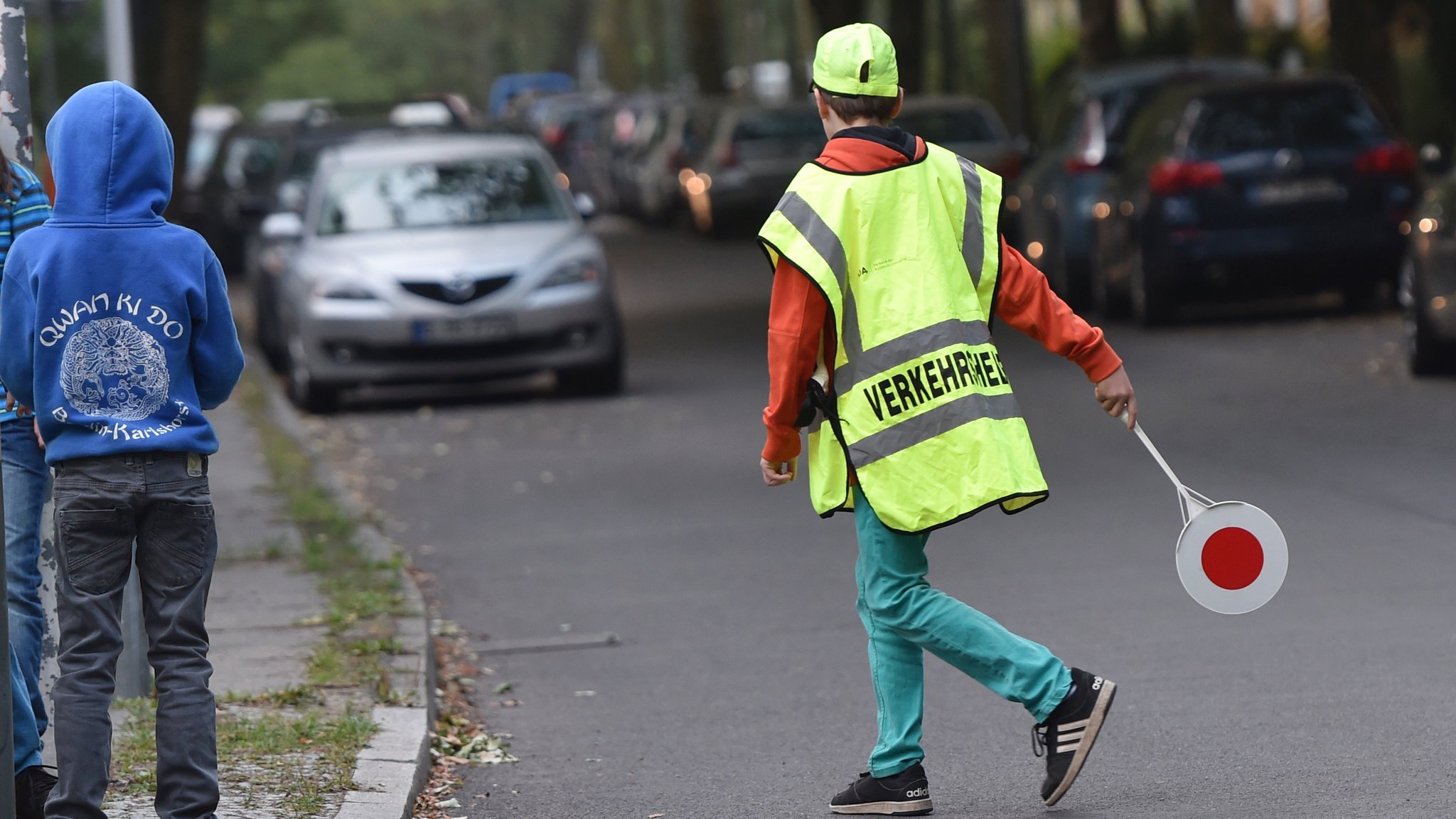 Ein Schulweghelfer sichert die Straße vor einer Schule.