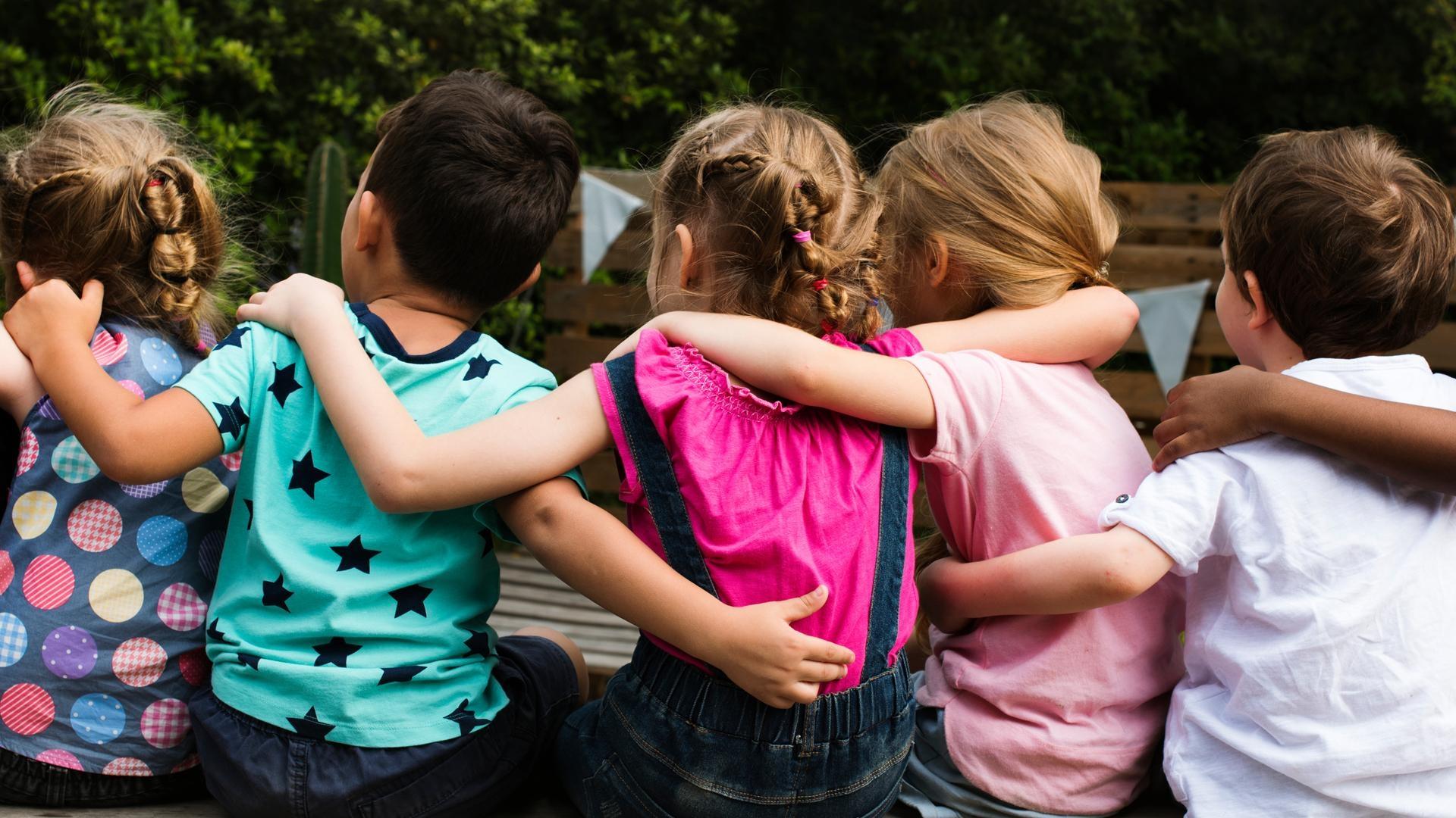 Die Rückansicht von fünf Kindern, die sitzend sich die Arme um die Schultern legen. (Symbolbild) Im Frühjahr ist in Bayern zum ersten Mal die verpflichtende Sprachstandserhebung durchgeführt worden bei Kindern, die nächstes Jahr im Herbst in die Schule sollen. Wie die Tests ausgefallen sind, hat das Kultusministerium jetzt bekannt gegeben. 
