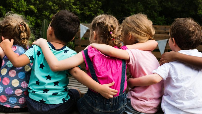 Die Rückansicht von fünf Kindern, die sitzend sich die Arme um die Schultern legen. (Symbolbild) Im Frühjahr ist in Bayern zum ersten Mal die verpflichtende Sprachstandserhebung durchgeführt worden bei Kindern, die nächstes Jahr im Herbst in die Schule sollen. Wie die Tests ausgefallen sind, hat das Kultusministerium jetzt bekannt gegeben. | Bild: Bayerischer Rundfunk 2025 Die Rückansicht von fünf Kindern, die sitzend sich die Arme um die Schultern legen. (Symbolbild) Im Frühjahr ist in Bayern zum ersten Mal die verpflichtende Sprachstandserhebung durchgeführt worden bei Kindern, die nächstes Jahr im Herbst in die Schule sollen. Wie die Tests ausgefallen sind, hat das Kultusministerium jetzt bekannt gegeben.
