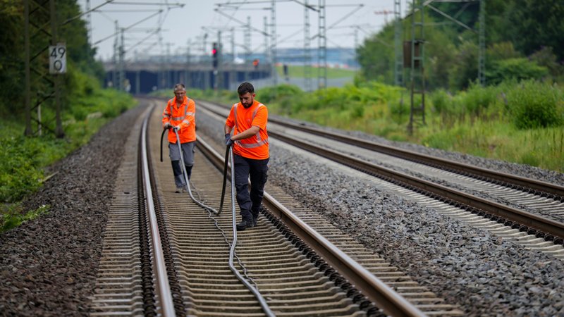 wei Mitarbeiter der Deutschen Bahn mit einem neuen Kabel, das an einem Gleisabschnitt in Düsseldorf verlegt werden soll, nachdem neben der Bahnstrecke Feuer in einem Kabeltunnel gelegt wurde. | Bild: dpa-Bildfunk/Christoph Reichwein wei Mitarbeiter der Deutschen Bahn mit einem neuen Kabel, das an einem Gleisabschnitt in Düsseldorf verlegt werden soll, nachdem neben der Bahnstrecke Feuer in einem Kabeltunnel gelegt wurde.