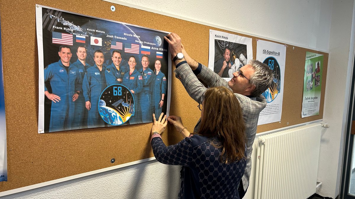 Schulleiter Franz Eisentraut und Lehrerin Birgit Reisner hängen im GCE in Bayreuth ein Plakat auf, das Astronauten zeigt.