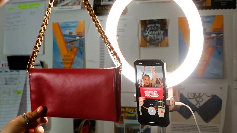 (Symbolbild) Eine junge Frau hält eine rote Tasche in die Frontkamera ihres Handys. | Bild: picture alliance / ASSOCIATED PRESS | Noah K. Murray (Symbolbild) Eine junge Frau hält eine rote Tasche in die Frontkamera ihres Handys.