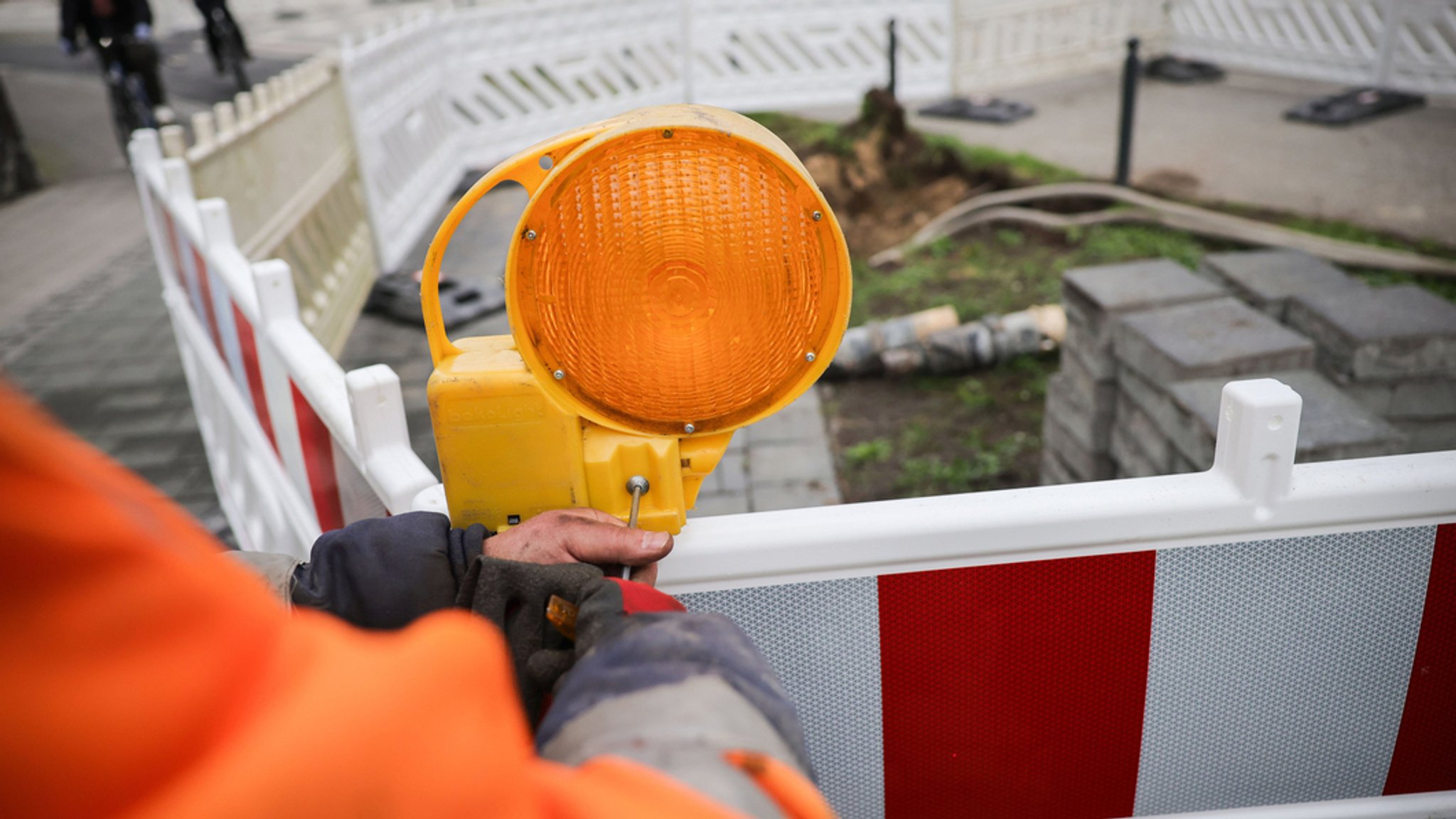 Ein Arbeiter sichert eine Baustelle mit Warnlampen am Absperrzaun (Symbolbild)