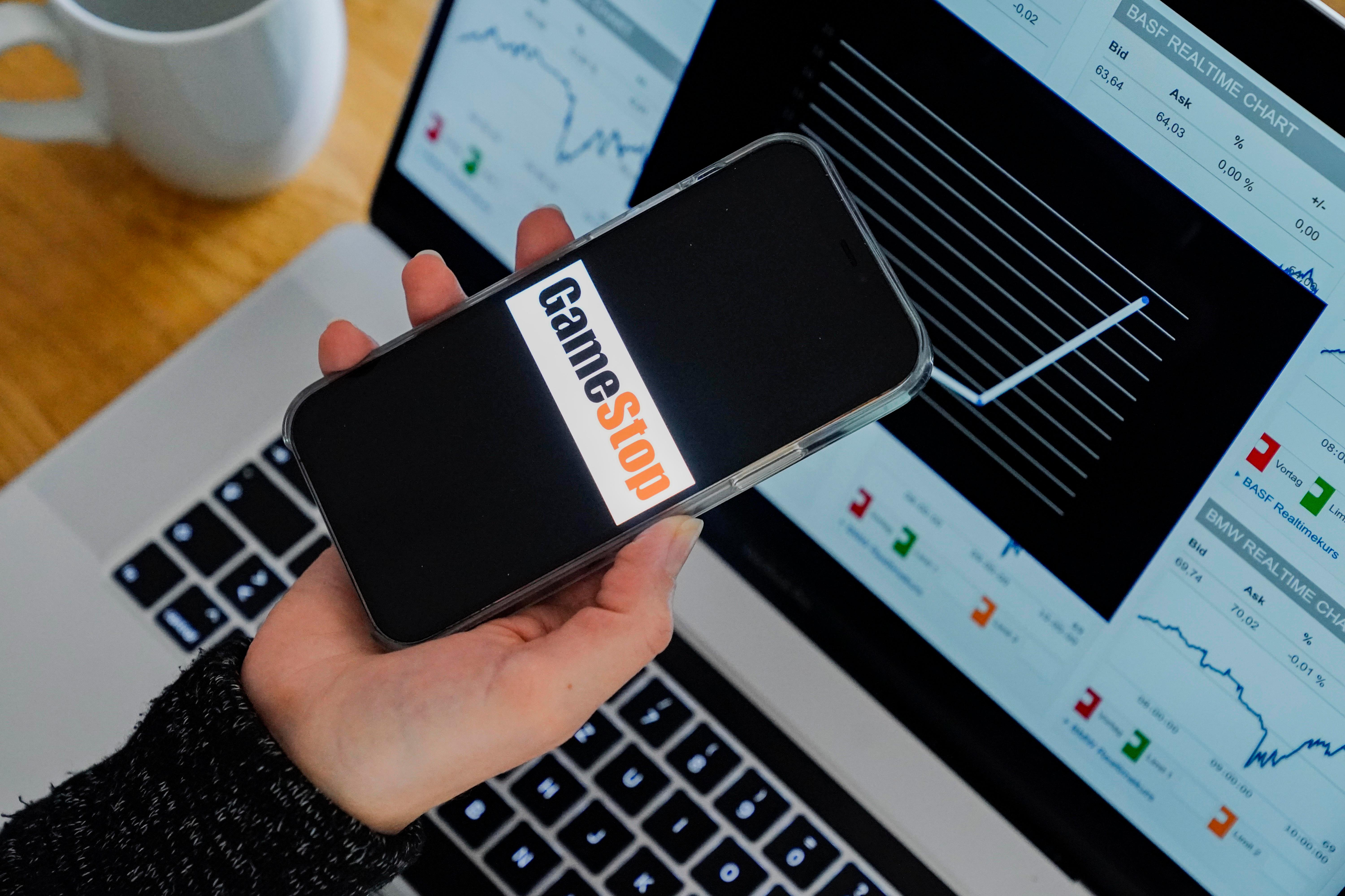 Eine junge Frau mit Smartphone und Laptop checkt den aktuellen GameStop-Kurs.