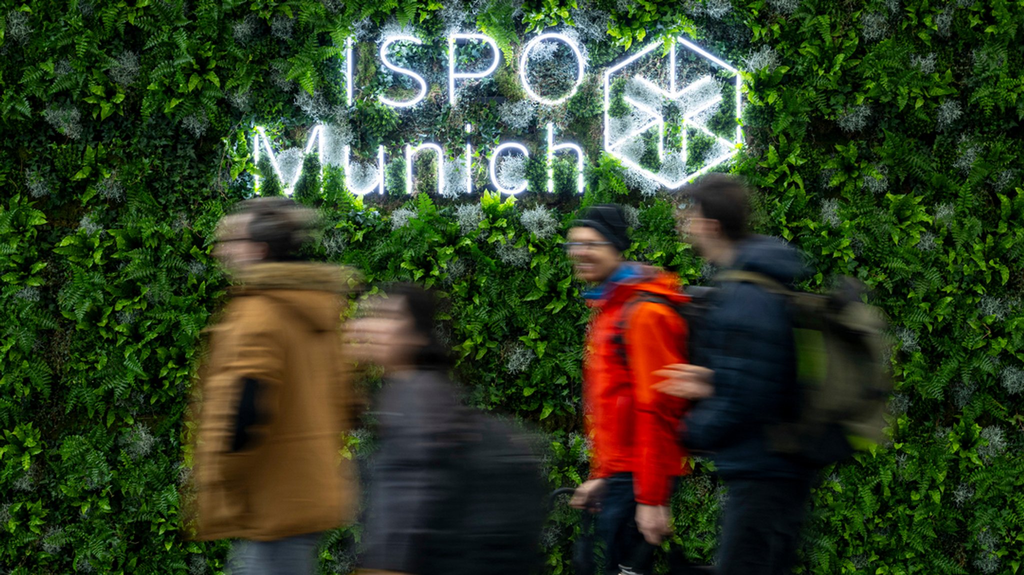 Besucher gehen während der Sportartikelmesse ISPO in der Messe München am Logo "ISPO Munich" vorbei