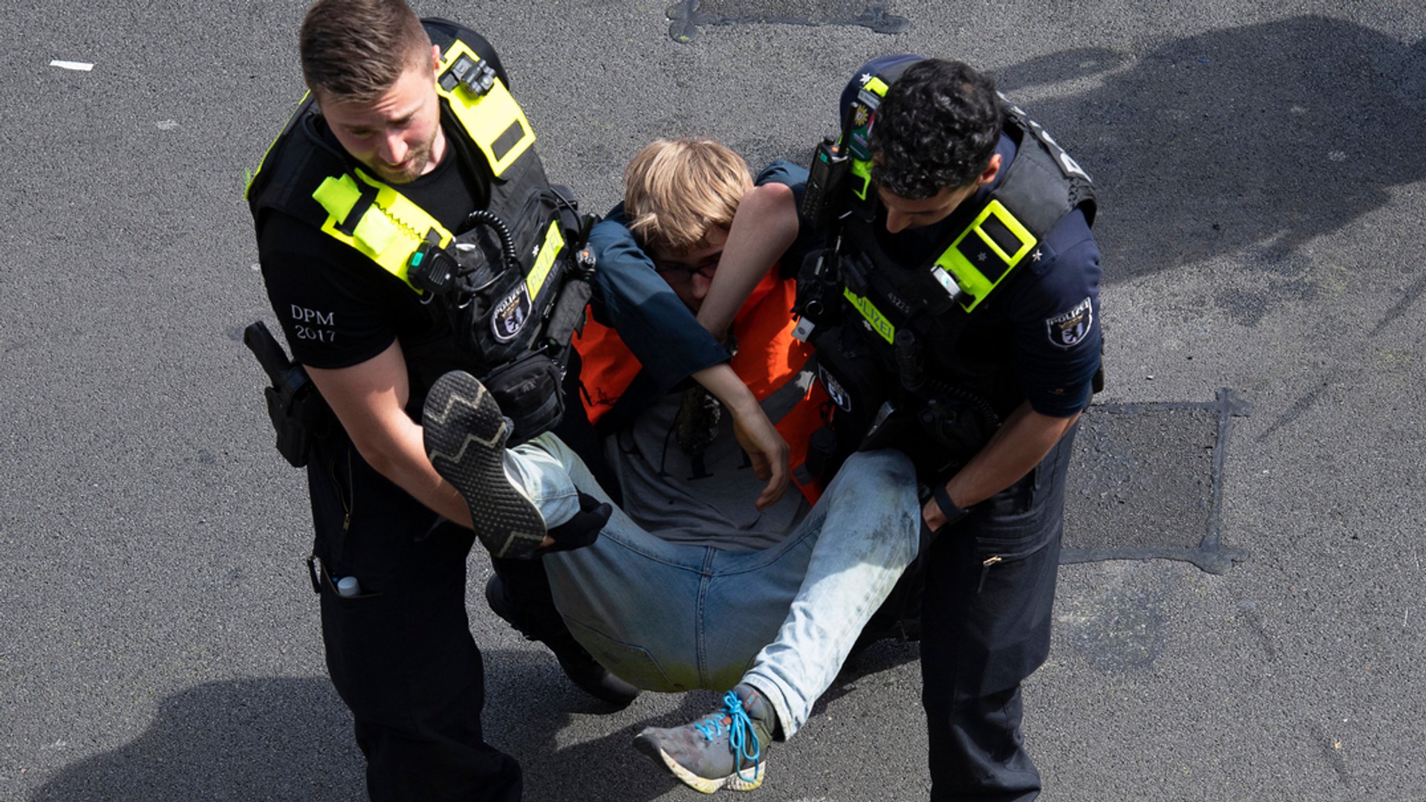 22.05.2023, Berlin: Polizeibeamte tragen bei einer Blockade der "Letzten Generation" auf der Autobahn 100 einen Aktivisten von der Straße. 