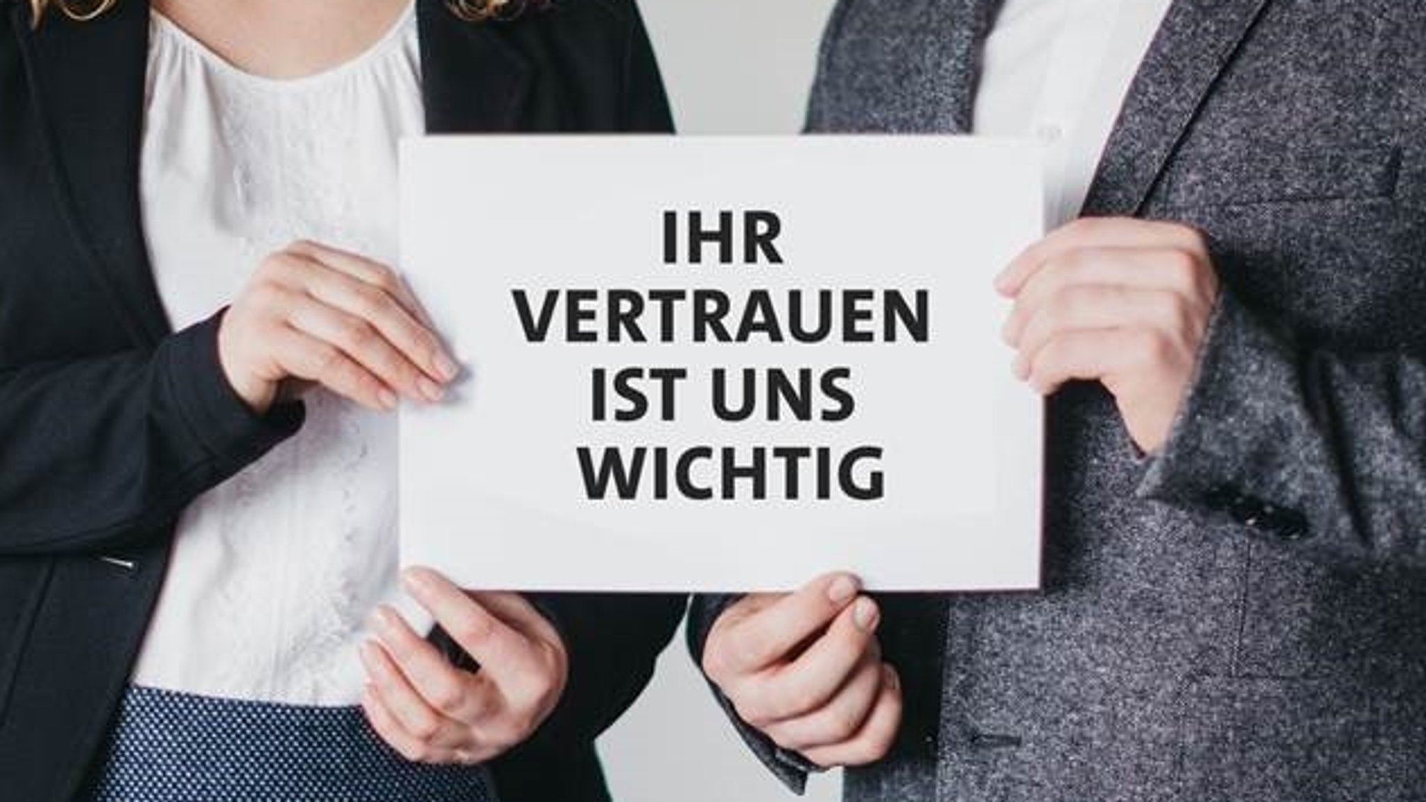 "Ihr Vertrauen ist uns wichtig" steht auf einer Tafel, die von zwei Menschen hochgehalten wird 