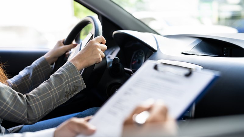 Eine junge Frau am Steuer eines Autos, der Beifahrer füllt ein Formular aus. | Bild: stock.adobe.com/Andrey Popov Eine junge Frau am Steuer eines Autos, der Beifahrer füllt ein Formular aus.