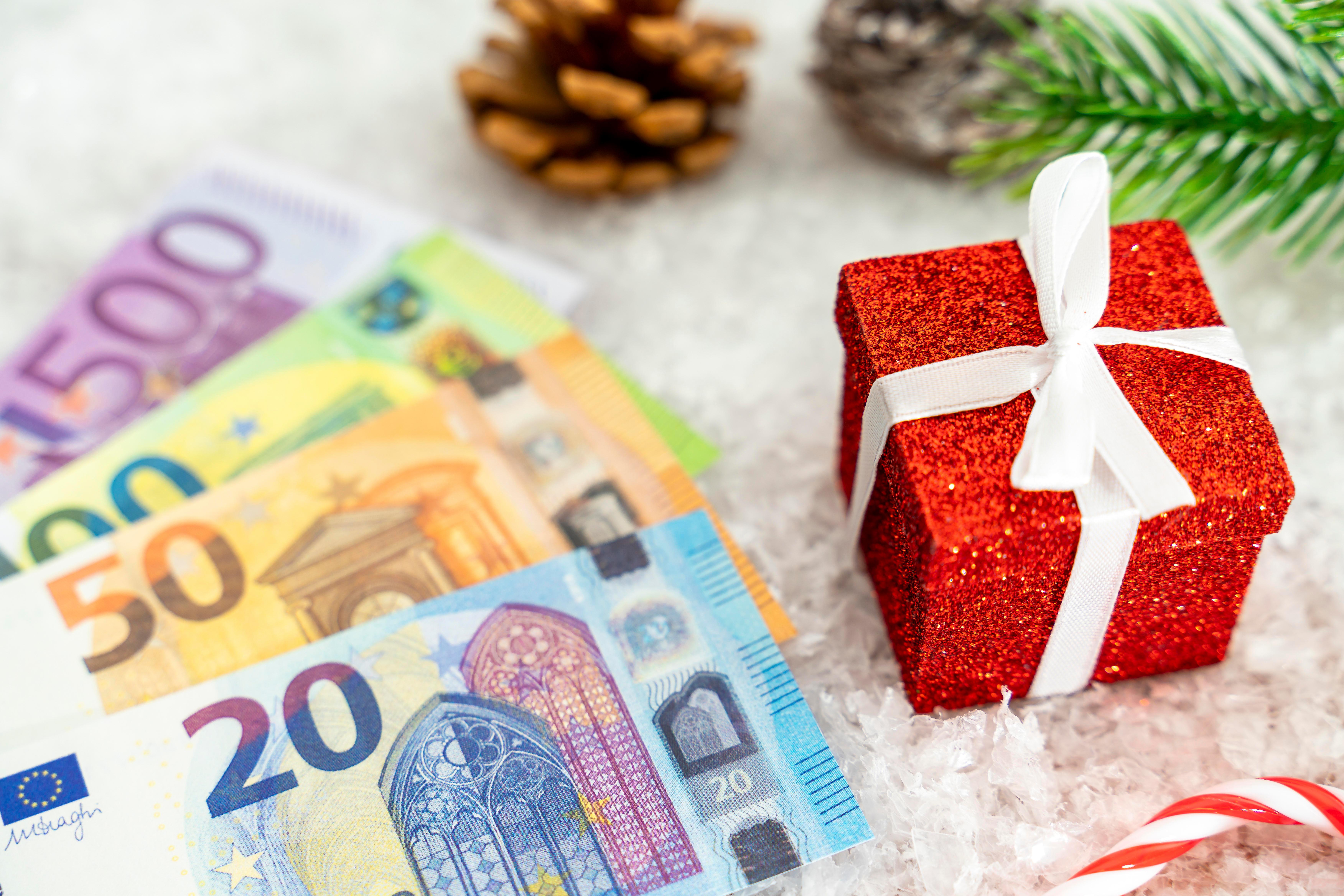 Geld mit Weihnachts-Elementen: Einem roten Geschenk, Kunstschnee, Tannenzweig und Tannenzapfen