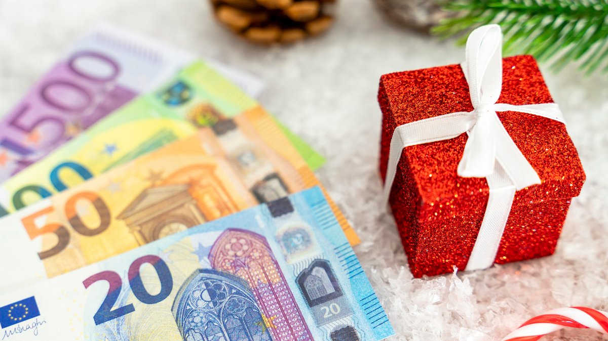 Geld mit Weihnachts-Elementen: Einem roten Geschenk, Kunstschnee, Tannenzweig und Tannenzapfen
