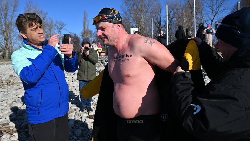 Eisschwimmer Paul Bieber (M) geht nach seinem Rekord im Eisschwimmen im Bodensee, bei dem er von Rettungsschwimmern im Boot begleitet wurde, an Land. 