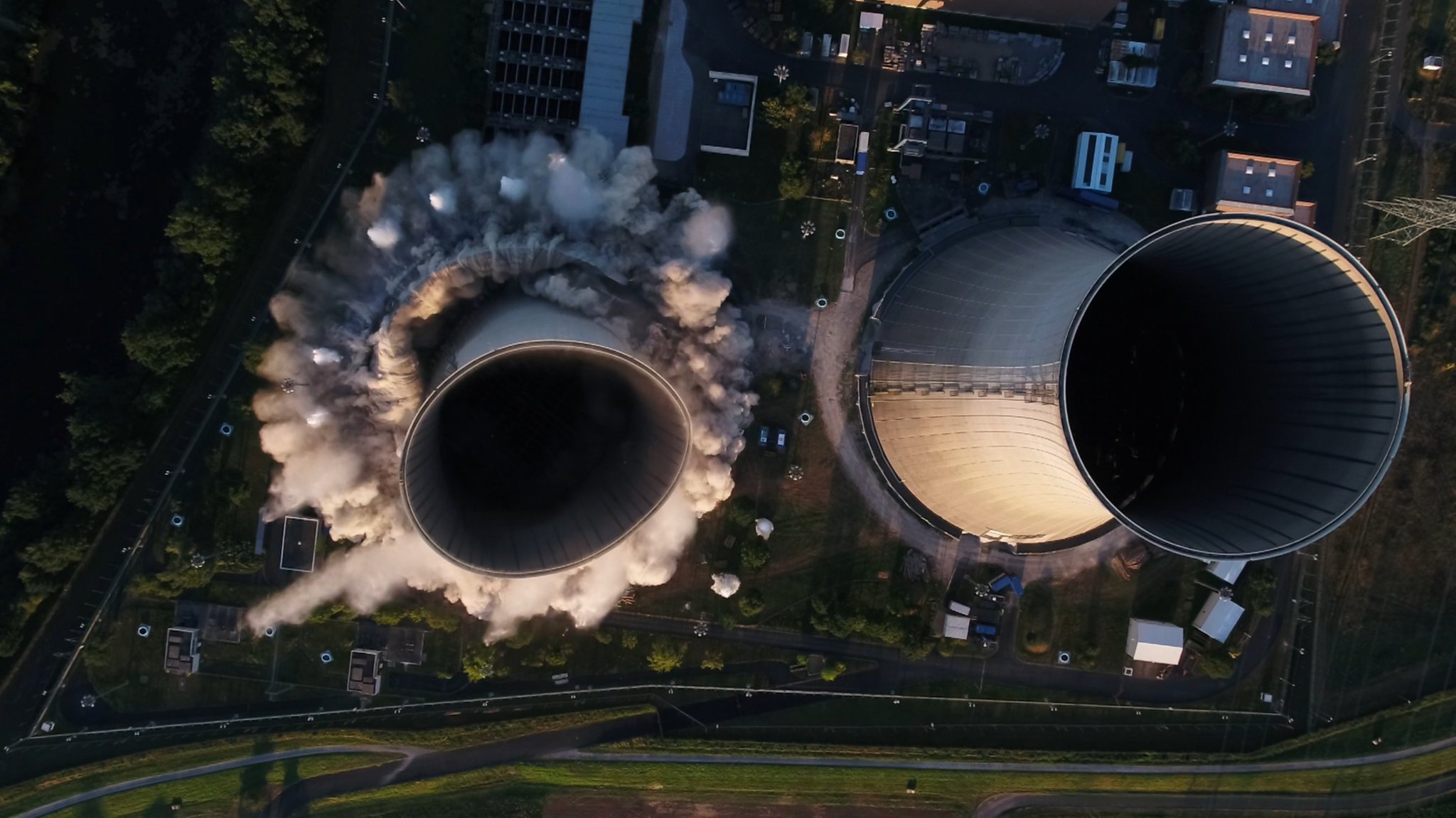 16.08.2024, Bayern, Grafenrheinfeld: Ein Kühlturm des stillgelegten Kernkraftwerkes stürzt nach der Sprengung zusammen.