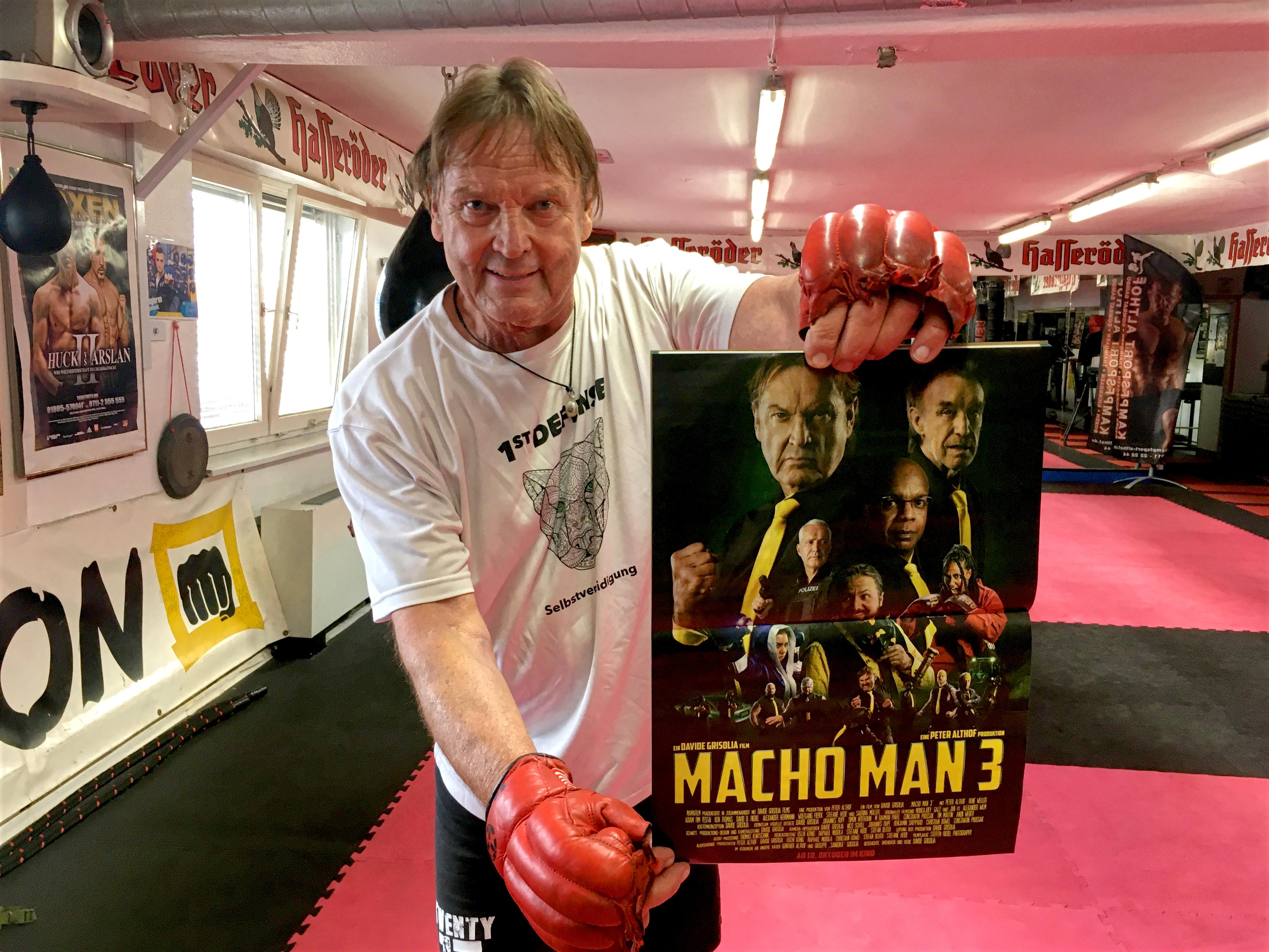 Peter Althof, Personenschützer, hält ein Plakat zu Macho Man 3 in die Kamera.