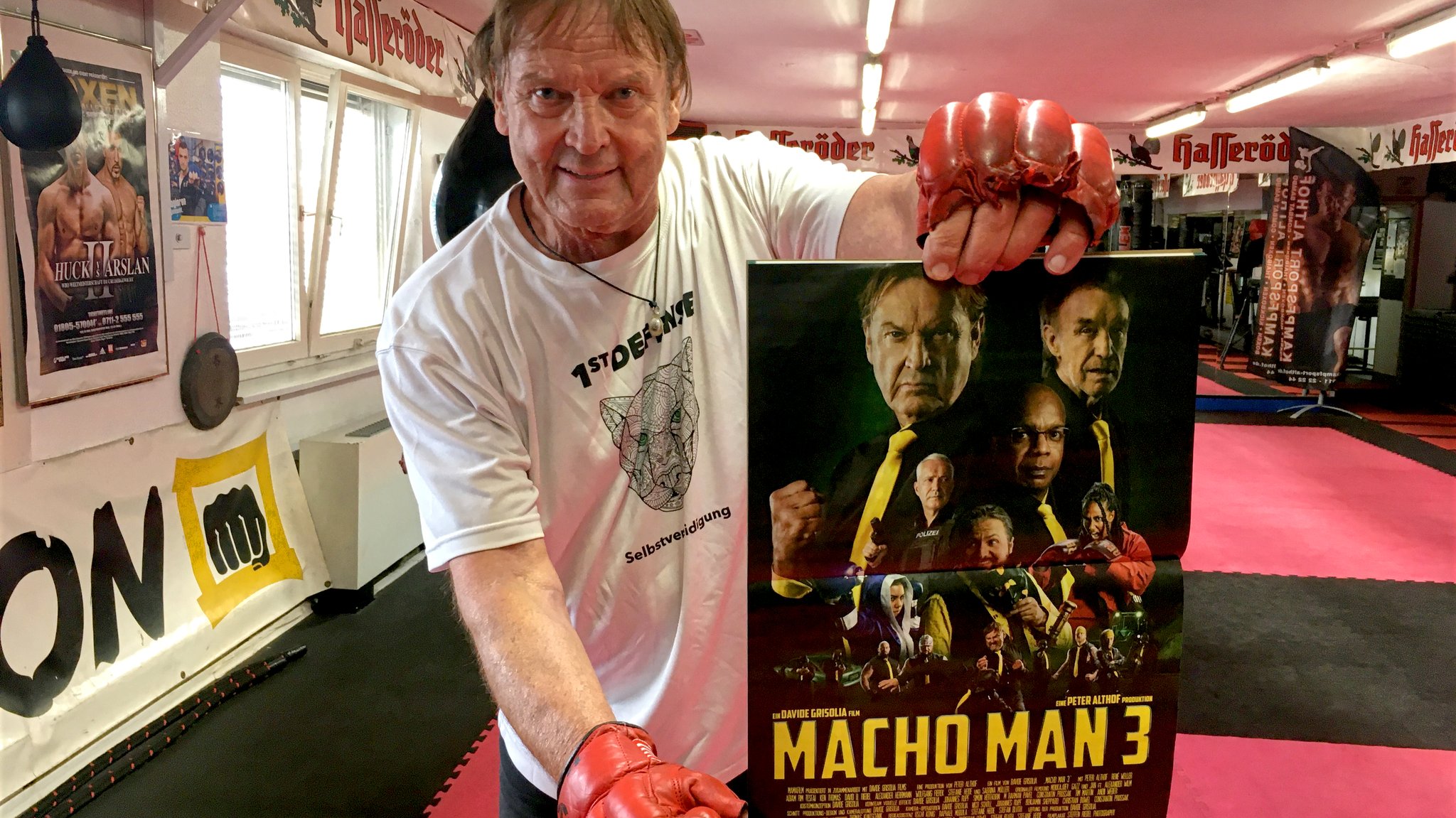 Peter Althof, Personenschützer, hält ein Plakat zu Macho Man 3 in die Kamera.