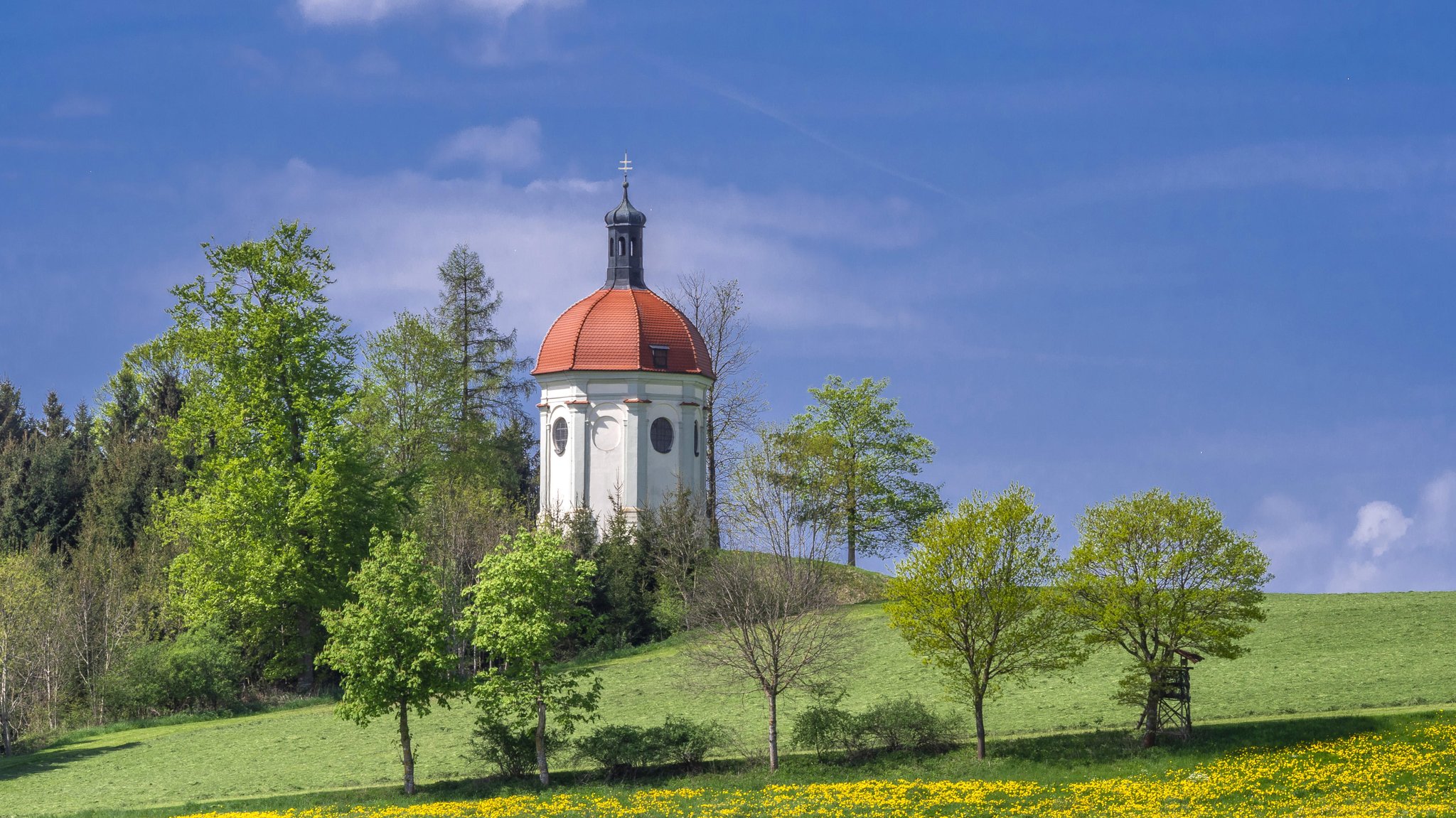 Eine kleine Kapelle auf einem Hügel von Bäumen umgeben. 