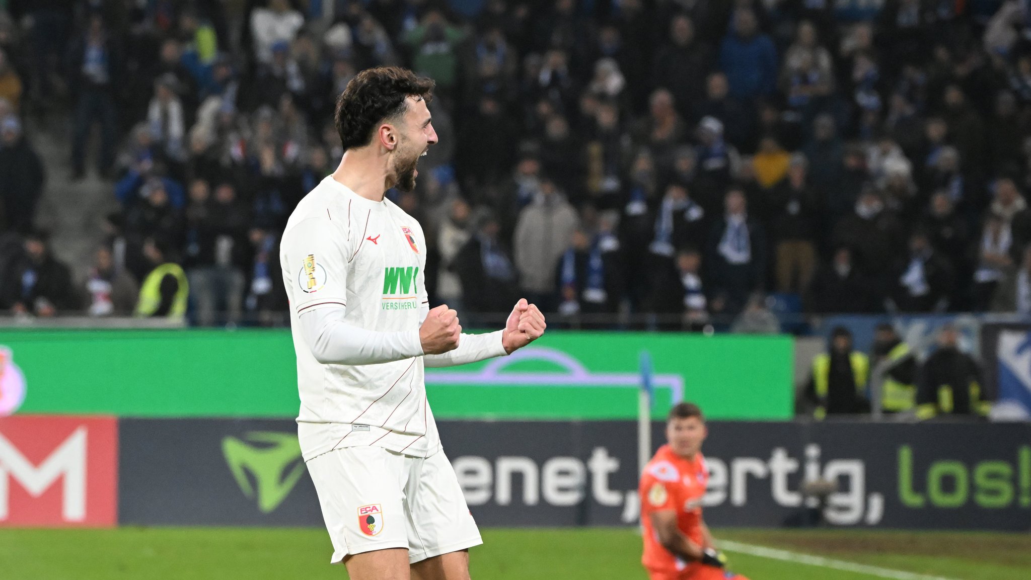 04.12.2024, Baden-Württemberg, Karlsruhe: Fußball: DFB-Pokal, Karlsruher SC - FC Augsburg, Achtelfinale, BBBank Wildpark. Der Augsburger Maximilian Bauer bejubelt seinen Siegtreffer zum 4:5 im Elfmeterschiessen. Der Karlsruher Torwart Max Weiß hockt dahinter am Boden. Foto: Uli Deck/dpa - WICHTIGER HINWEIS: Gemäß den Vorgaben der DFL Deutsche Fußball Liga bzw. des DFB Deutscher Fußball-Bund ist es untersagt, in dem Stadion und/oder vom Spiel angefertigte Fotoaufnahmen in Form von Sequenzbildern und/oder videoähnlichen Fotostrecken zu verwerten bzw. verwerten zu lassen. +++ dpa-Bildfunk +++