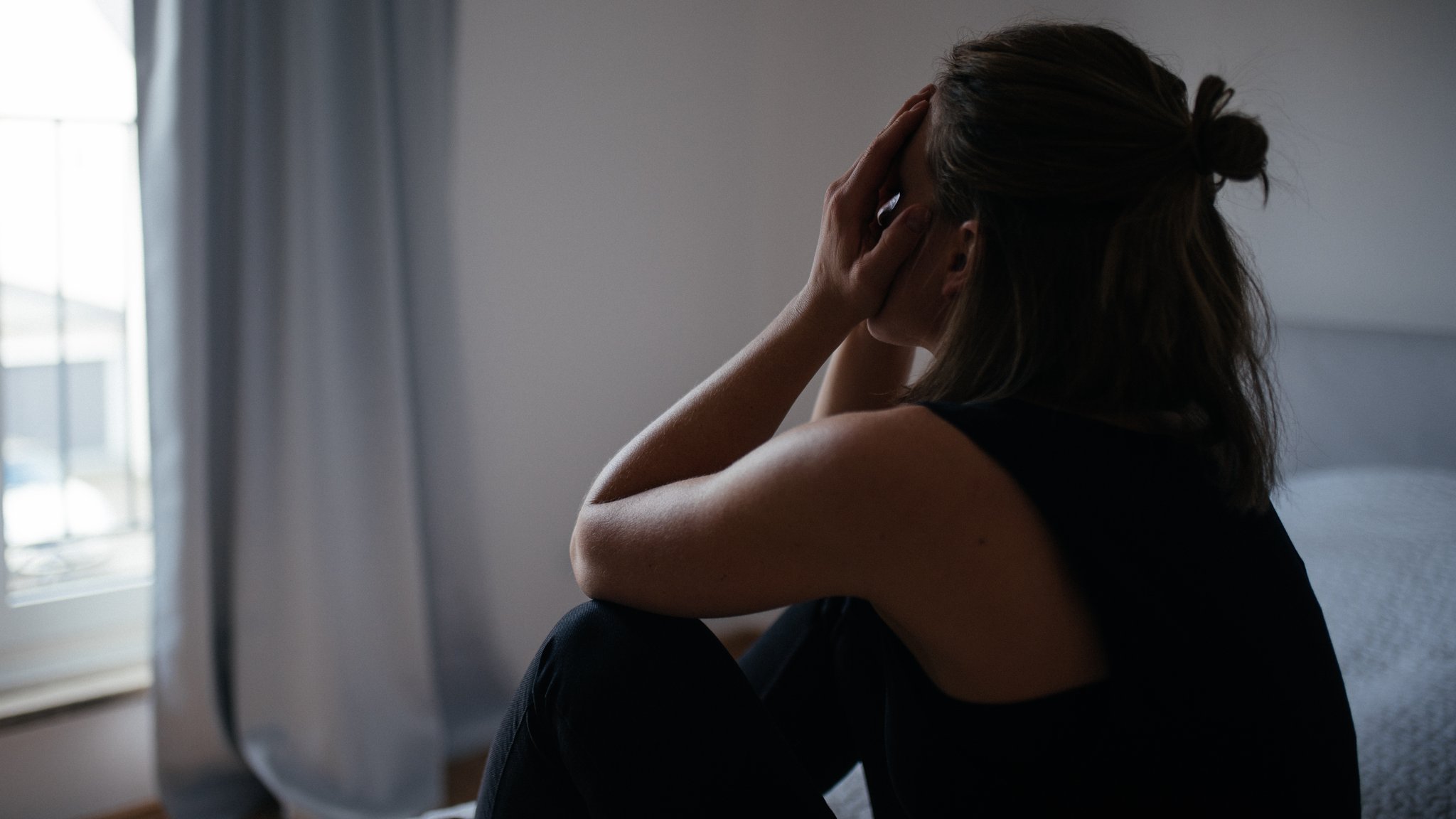 Eine Frau sitzt auf einem Bett und hält sich die Hände vor das Gesicht.