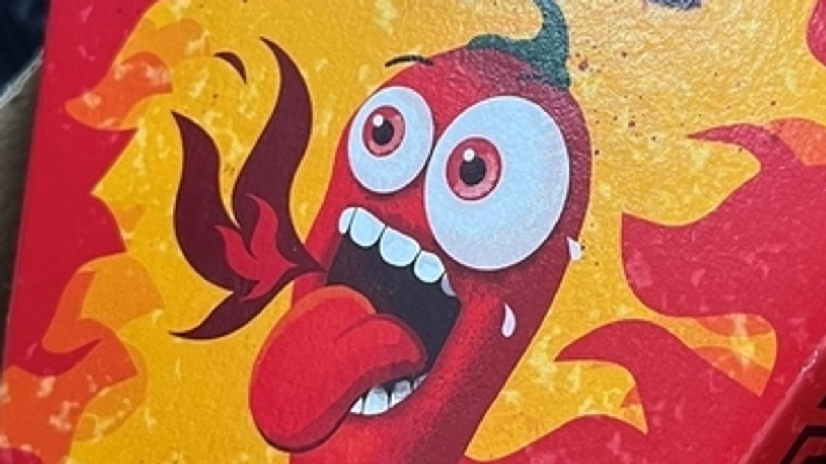 Auf der Verpackung der Tortilla-Chips ist eine Chilischote mit weit aufgerissenen Augen abgebildet, offenem Mund mit herausgestreckter Zunge und einer Flamme vor dem Mund.