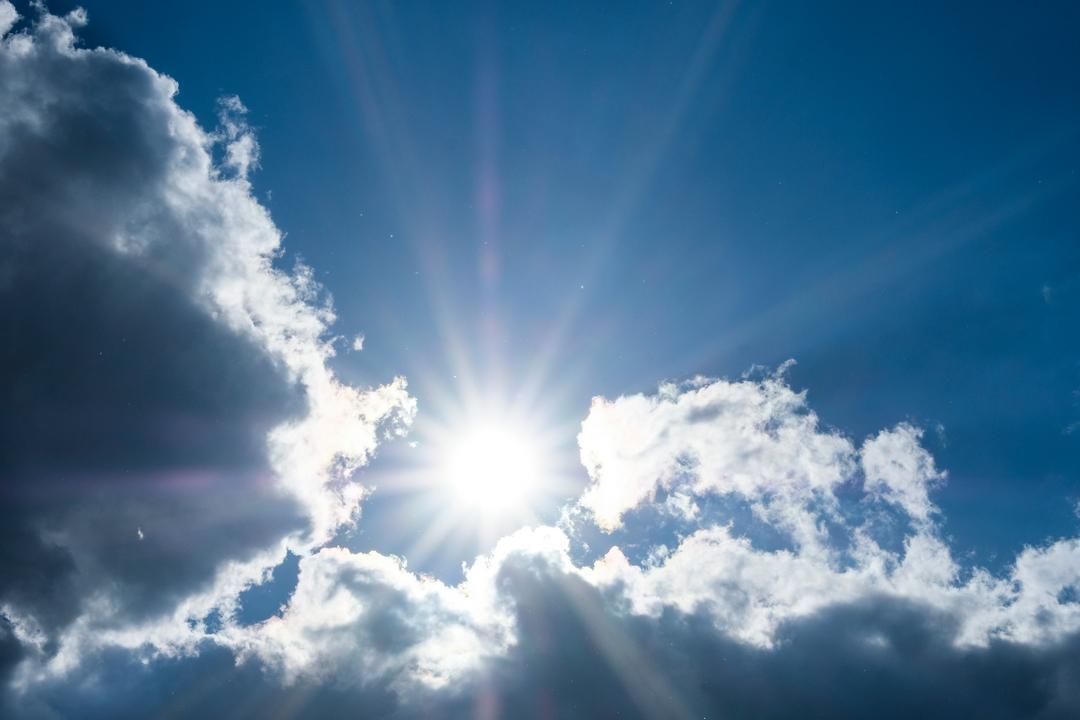 Grelle Sonne vor blauem Himmel von dunklen Wolken umrahmt