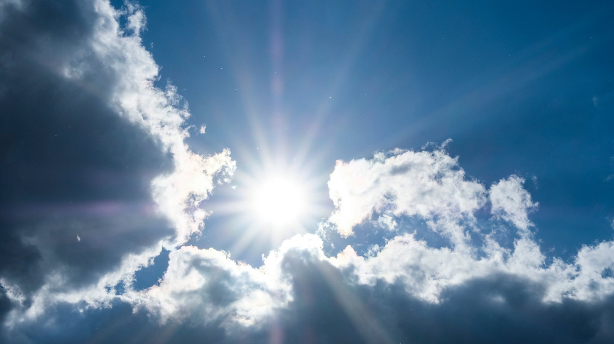 Grelle Sonne vor blauem Himmel von dunklen Wolken umrahmt