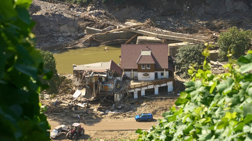 Rheinland-Pfalz, Marienthal: Ein Haus ist nach dem Hochwasser vollkommen aufgerissen, dahinter ist eine zerstörte Brücke zu sehen.